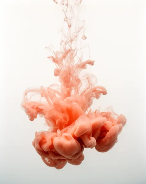 Coral-colored ink swirling in clear water against a white background, forming intricate patterns and textures.