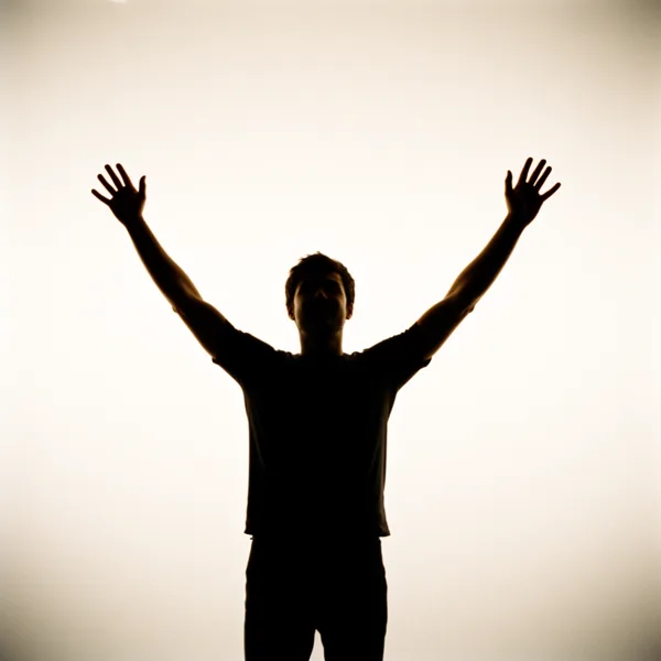Silhouette of a person with arms raised against a bright backlit background.