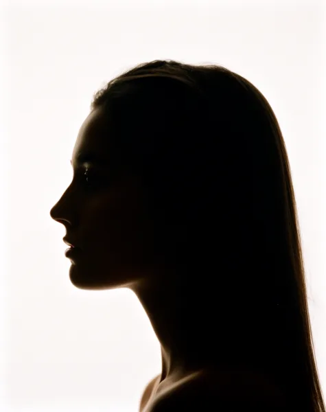 Silhouette of a woman's profile with long hair against a bright white background, creating a high contrast image.