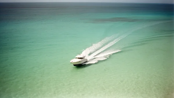 Aerial view of a speedboat moving on turquoise sea with a white wake behind it under natural lighting.