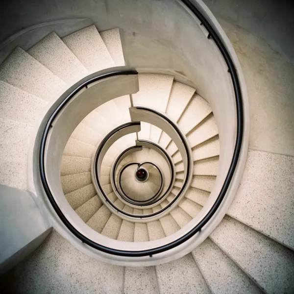 Top view of a spiral staircase with curved railing and textured steps, illuminated by soft lighting.