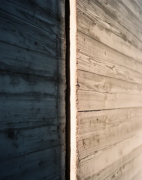 Close-up view of a textured concrete wall with a vertical gap, one side in sunlight and the other in shadow.