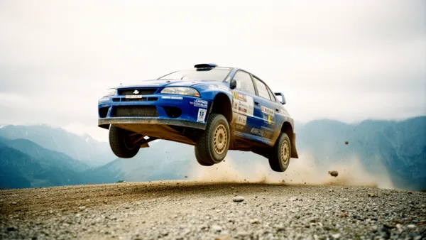 Blue rally car airborne on gravel track with mountains in the background and dust trailing behind.