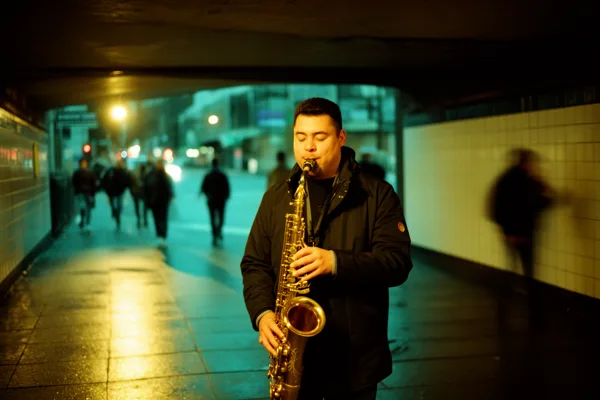 A saxophonist plays in a dimly lit urban tunnel with blurred pedestrians in the background.