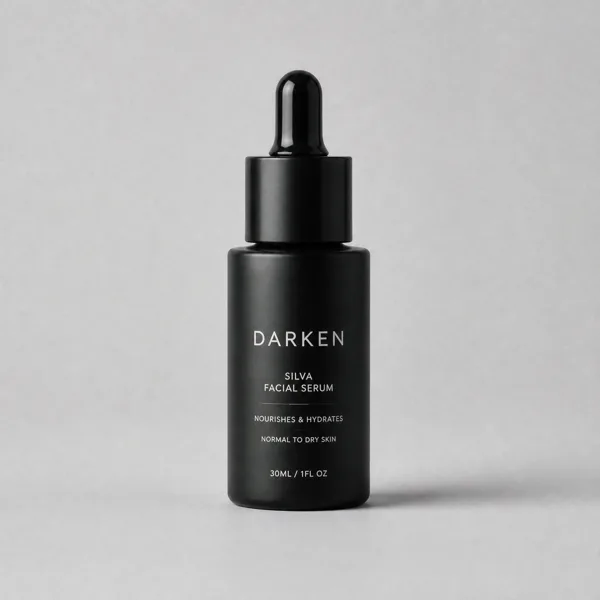A black facial serum bottle with a dropper cap on a gray background, casting a soft shadow.