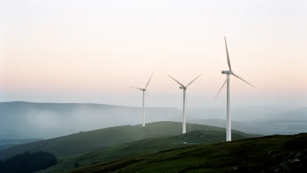 Three wind turbines on green hills with a pastel sky at dusk, creating a serene and sustainable energy scene.