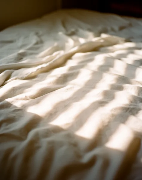 Close-up of wrinkled bed sheets with sunlight casting shadows, creating a textured appearance.