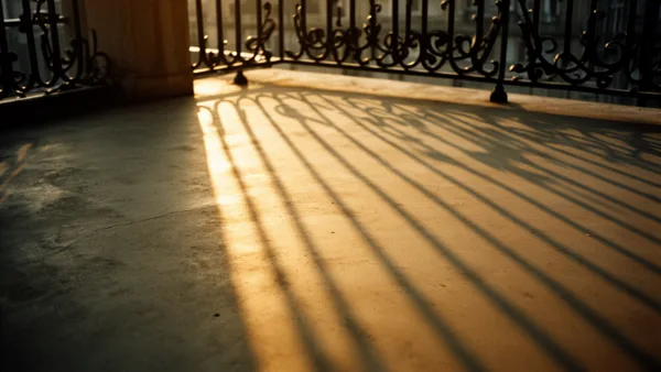 Shadows of a wrought iron balcony railing cast on a concrete floor with warm golden light.
